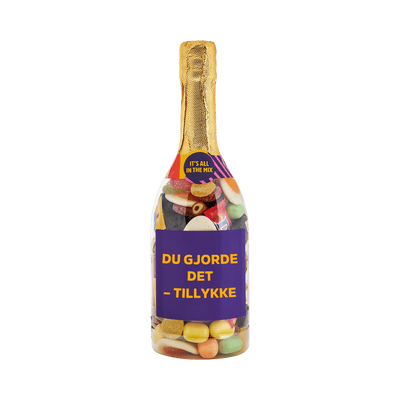 Champagneflaske fyldt med slik og lilla etiket med teksten "Du gjorde det – tillykke" – sød gave fra SlikEkspressen.