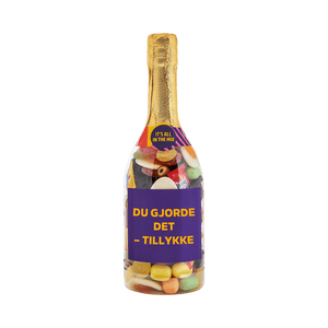 Champagneflaske fyldt med slik og lilla etiket med teksten "Du gjorde det – tillykke" – sød gave fra SlikEkspressen.