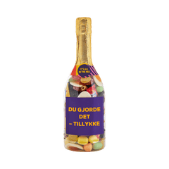 Champagneflaske fyldt med slik og lilla etiket med teksten "Du gjorde det – tillykke" – sød gave fra SlikEkspressen.